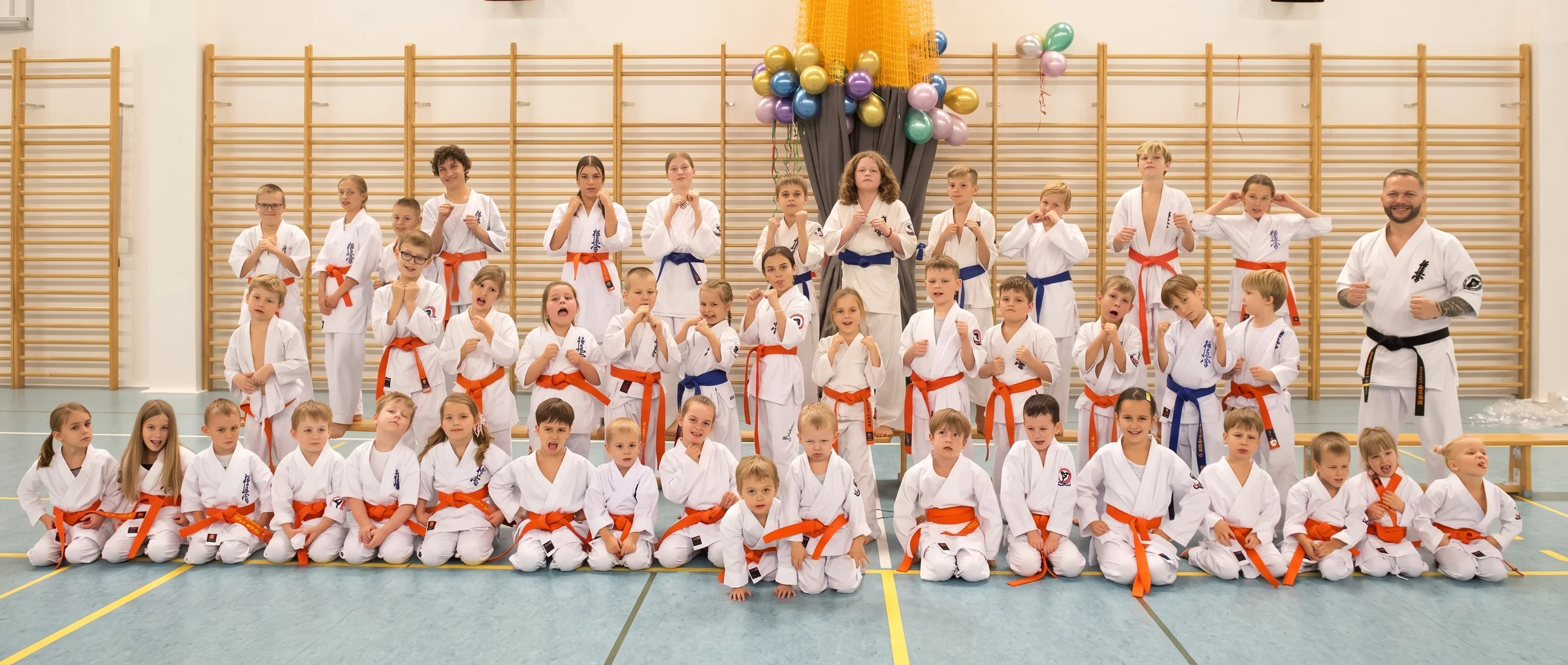 Wspólne zdjęcie Tynieckiego Klubu Karate: kilkadziesiąt dzieci i trener na hali