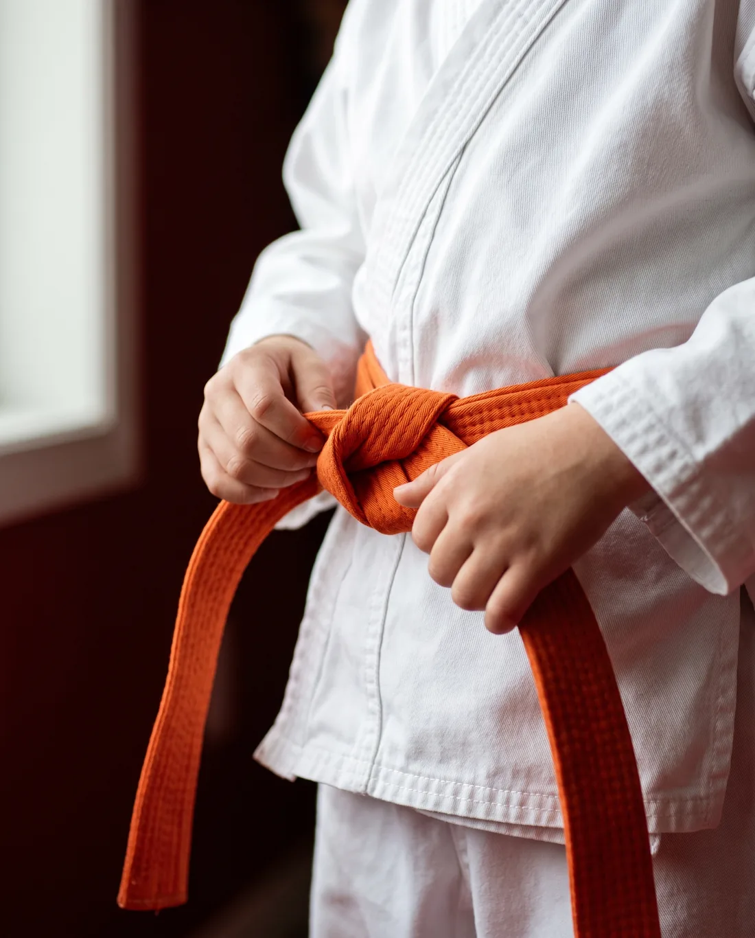 Dziecko w białym karate gi zawiązuje pomarańczowy pas